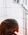 Person shampooing hair under a shower with a filter, enjoying a luxurious water experience.